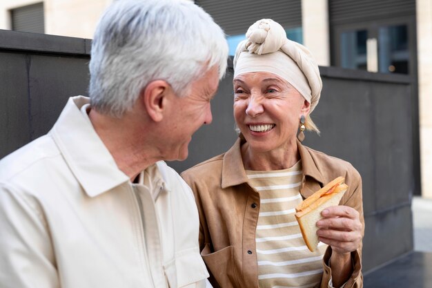 Sonriente pareja de ancianos al aire libre disfrutando de un sándwich juntos