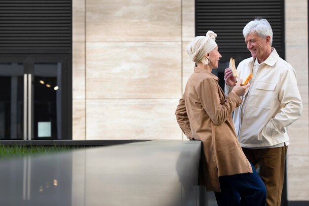 Sonriente pareja de ancianos al aire libre disfrutando de un sándwich juntos