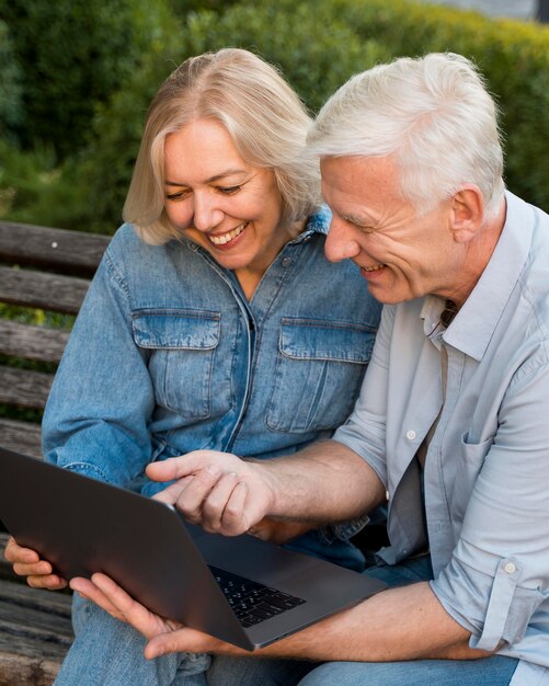Sonriente pareja de ancianos al aire libre con un portátil en un banco