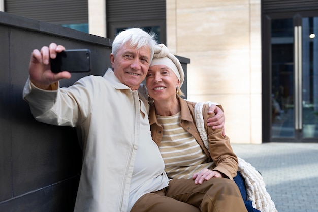 Sonriente pareja de ancianos al aire libre tomando un selfie junto con el teléfono inteligente