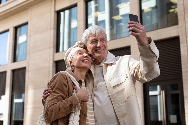 Sonriente pareja de ancianos al aire libre tomando un selfie junto con el teléfono inteligente