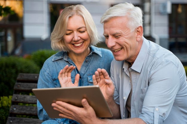 Sonriente pareja de ancianos saludando a alguien con quien están hablando en tableta