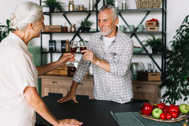 Sonriente pareja de ancianos tostado bebidas alcohólicas en la cocina