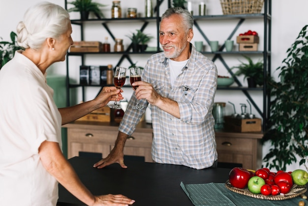 Sonriente pareja de ancianos tostado bebidas alcohólicas en la cocina