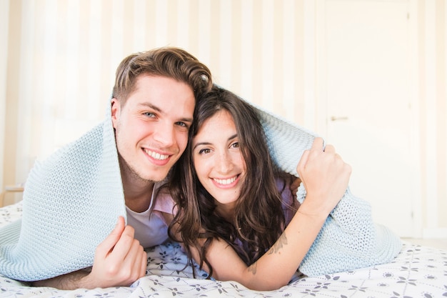 Sonriente pareja debajo de la manta