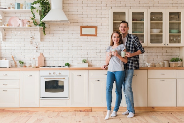 Sonriente pareja descansando en la cocina y saboreando el té