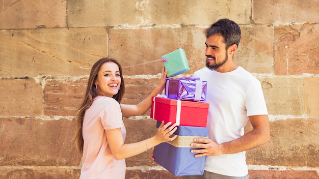 Sonriente pareja joven apilando regalos frente a la pared desgastada