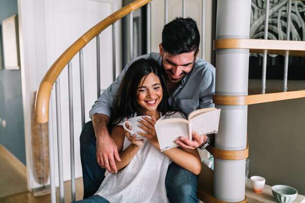 Sonriente, pareja joven, sentado, en, escalera, lectura, libro