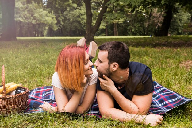 Sonriente pareja joven tumbado en la manta mirando el uno al otro en el picnic