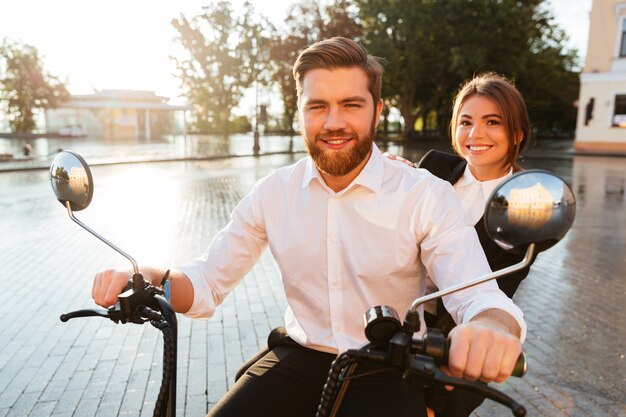 Sonriente pareja de negocios monta en moto moderna al aire libre