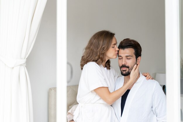 Sonriente pareja relajante y parejas abrazándose y besando la frente en la cama