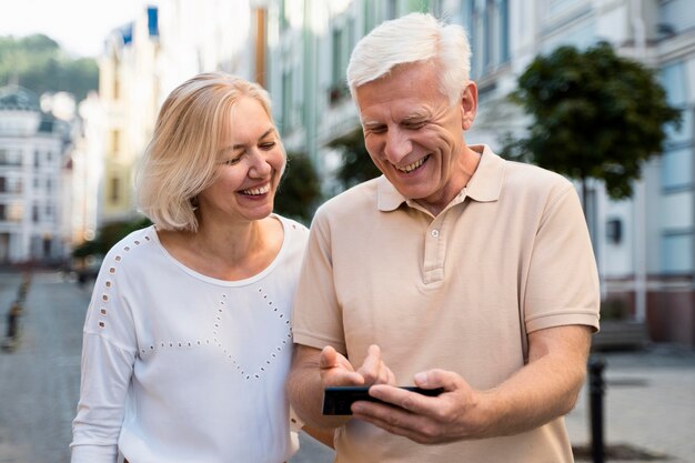 Sonriente pareja senior al aire libre en la ciudad con smartphone