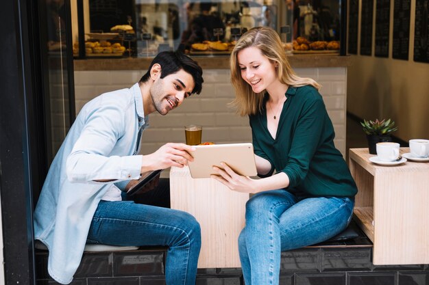 Sonriente pareja sentada en la cafetería con tableta