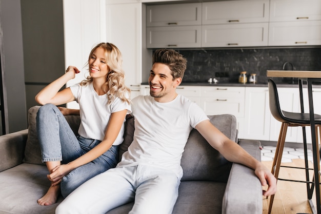 Foto gratuita sonriente pareja sentada en un sofá en apartamentos modernos y viendo la televisión. hombre joven alegre con su hermosa novia relajante en casa.