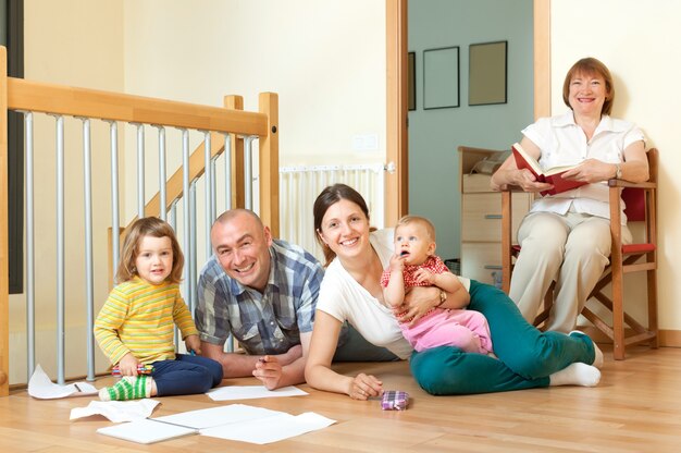 Sonriente pareja con sus hijos y abuela en piso en casa en sala de estar