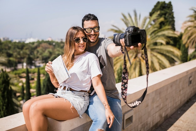 Sonriente pareja de turistas tomando autorretrato a través de la cámara