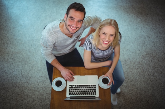 sonriente pareja usando la computadora portátil mientras que el café negro en la cafetería ©