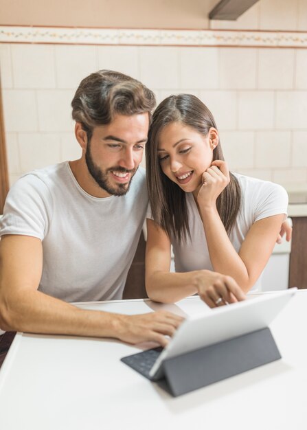 Sonriente pareja viendo la tableta en la mesa