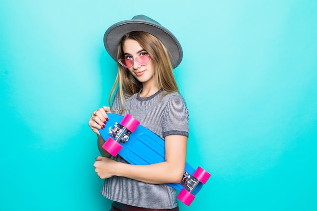 Sonriente skategirl adolescente se encuentra con patineta de colores aislado sobre fondo verde