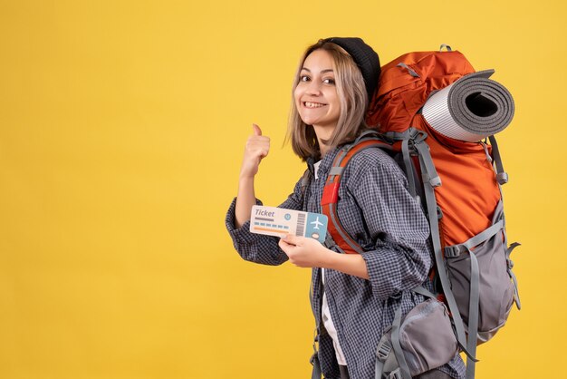 sonriente, viajero, mujer, con, mochila, tenencia, billete, señalar con dedo, atrás