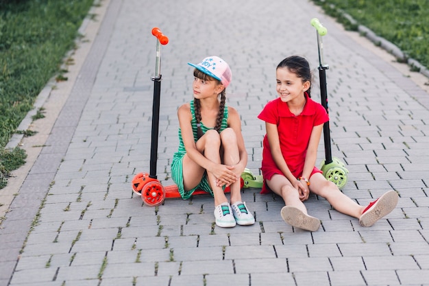 Foto gratuita sonrientes amigas sentadas en sus patadas en el parque