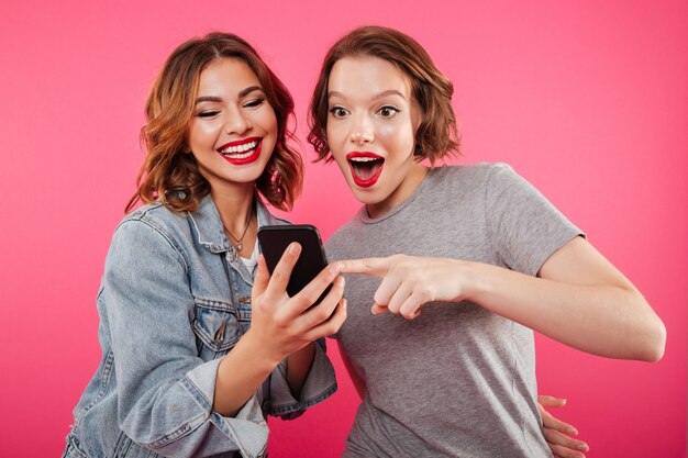 Sonrientes amigas mediante teléfono móvil.