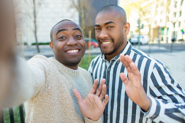 Sonrientes amigos afroamericanos saludando mientras toma selfie