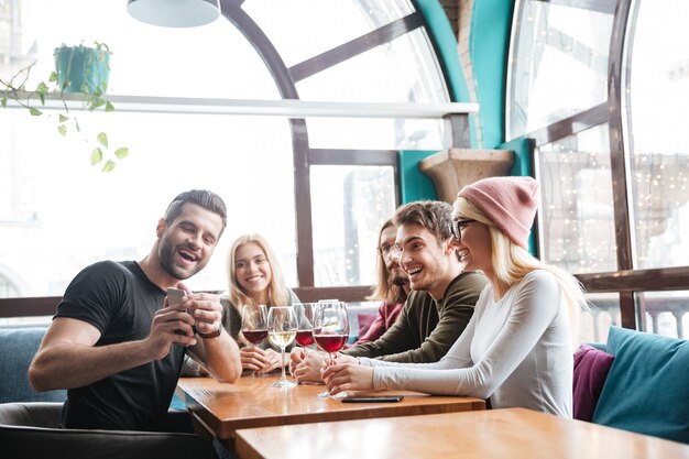 Sonrientes amigos en la cafetería bebiendo alcohol y hacer una selfie.