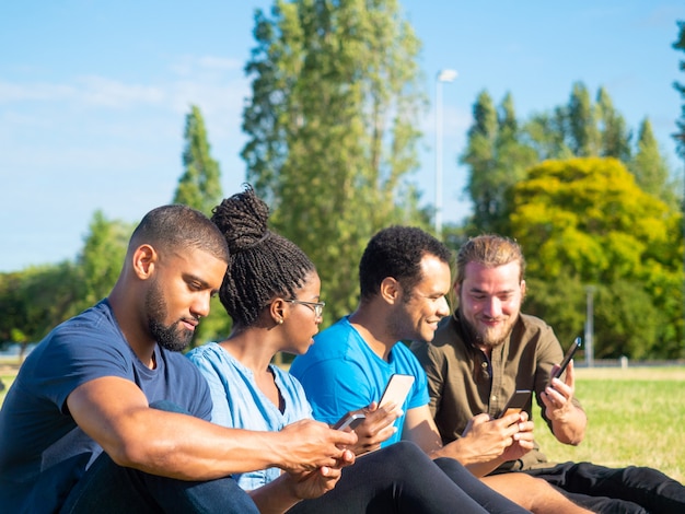 Sonrientes amigos usando teléfonos inteligentes en el parque