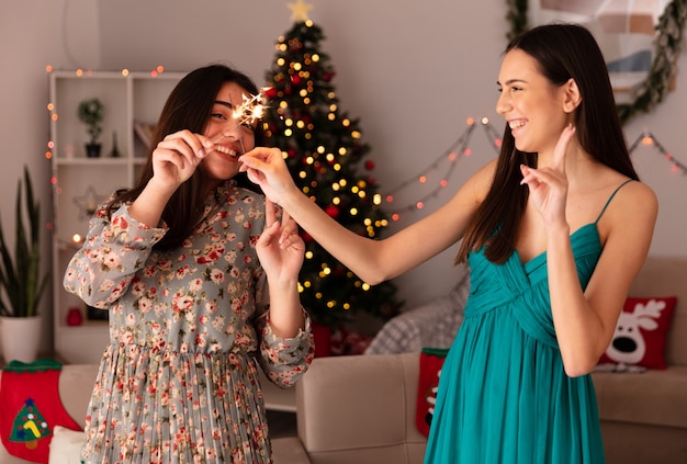 Foto gratuita sonrientes chicas guapas cruzando sus bengalas disfrutando de la navidad en casa