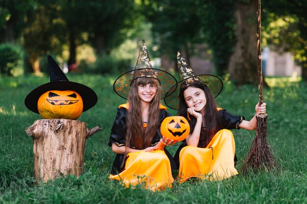 Sonrientes chicas en trajes de brujas sentados en el césped en el parque