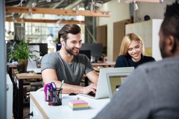 Sonrientes colegas jóvenes sentados en coworking de oficina