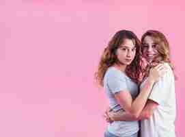 Foto gratuita sonrientes jóvenes amigas abrazándose contra el fondo rosa