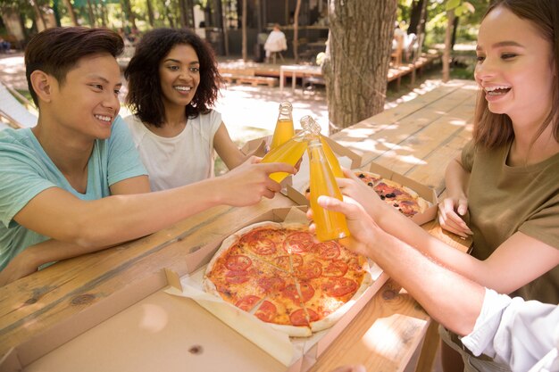 Sonrientes jóvenes amigos amigos multiétnicos al aire libre bebiendo jugo comiendo pizza.