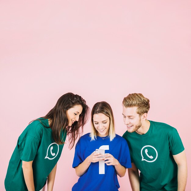 Sonrientes jóvenes amigos mirando smartphone contra fondo rosa