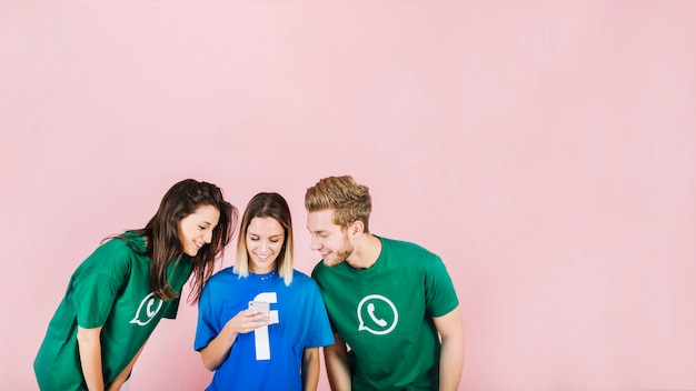 Foto gratuita sonrientes jóvenes amigos mirando smartphone contra fondo rosa