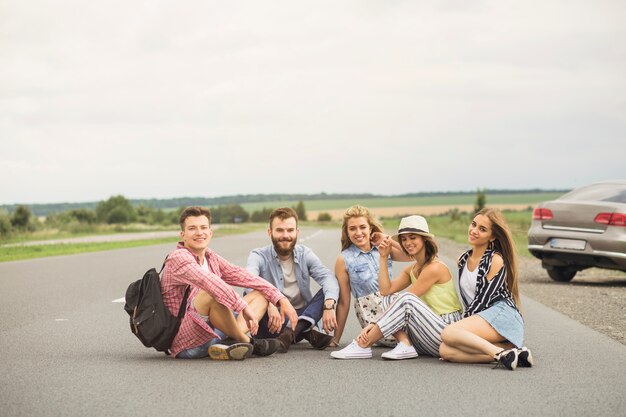 Sonrientes jóvenes amigos sentados en el camino rural