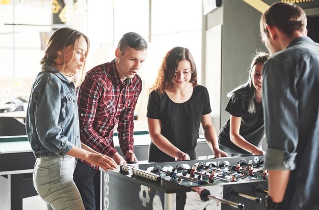 Sonrientes jóvenes jugando futbolín mientras están en el interior