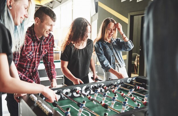 Sonrientes jóvenes jugando futbolín mientras están en el interior