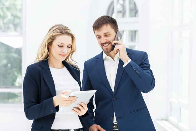 Los sonrientes trabajadores de oficina masculinos y femeninos con computadora portátil y teléfono