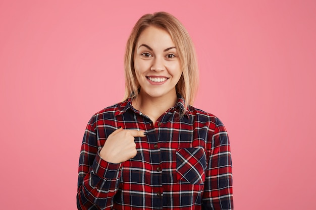 Una sonrisa agradable que se observa a sí misma con el dedo, vestida con una camisa a cuadros informal, de buen humor