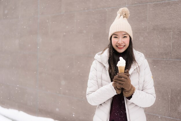 Sonrisa asiática joven hermosa de la mujer y feliz con helado en la estación del invierno de la nieve