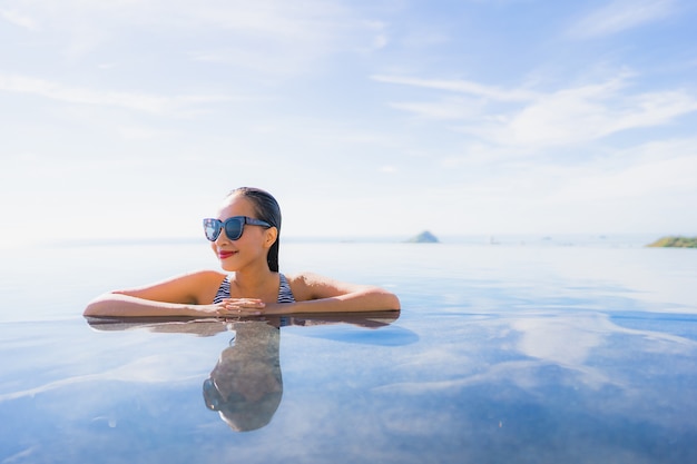 La sonrisa asiática joven hermosa de la mujer del retrato feliz se relaja alrededor de piscina en el centro turístico del hotel para el ocio