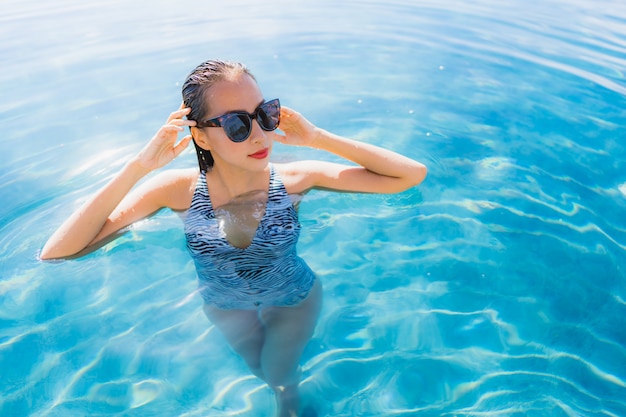 La sonrisa asiática joven hermosa de la mujer del retrato feliz se relaja alrededor de piscina en el centro turístico del hotel para el ocio