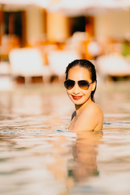 Foto gratuita la sonrisa asiática joven hermosa de la mujer del retrato feliz se relaja alrededor de piscina en el centro turístico del hotel para el ocio