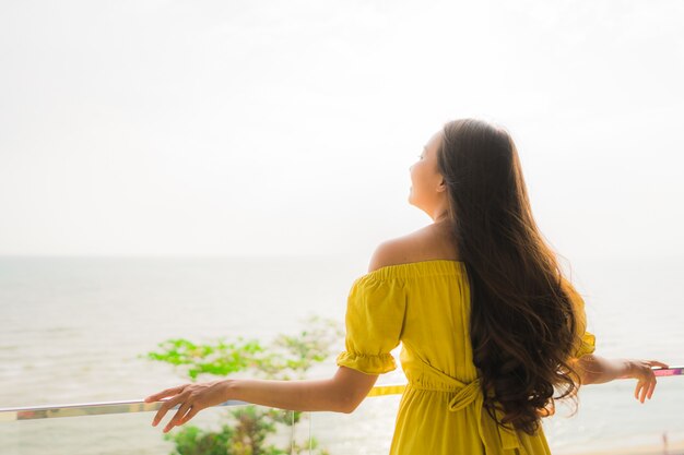 La sonrisa asiática joven hermosa de la mujer del retrato feliz y se relaja en el balcón al aire libre con la playa y el oce del mar