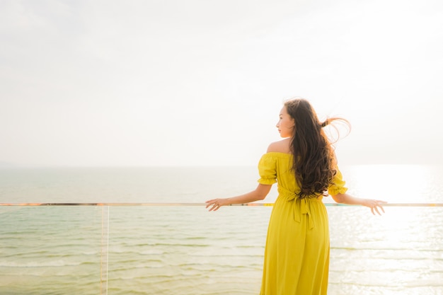 La sonrisa asiática joven hermosa de la mujer del retrato feliz y se relaja en el balcón al aire libre con la playa y el oce del mar