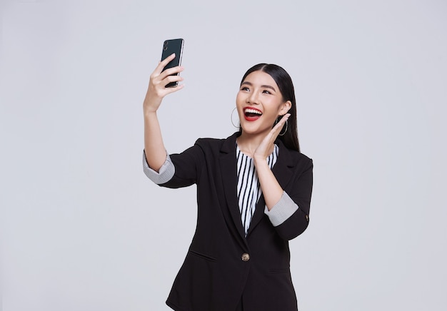 Sonrisa de empresaria asiática de cara feliz y amigable en traje formal que usa teléfono inteligente tiene una videollamada sobre fondo blanco foto de estudio.