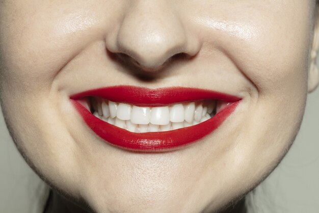 Sonrisa encantada. Sesión de primer plano de boca femenina con maquillaje de labios de brillo rojo brillante y piel de mejillas bien cuidada.