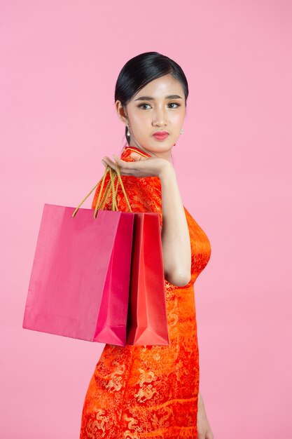 Sonrisa feliz hermosa mujer asiática y compras en año nuevo chino sobre fondo rosa.